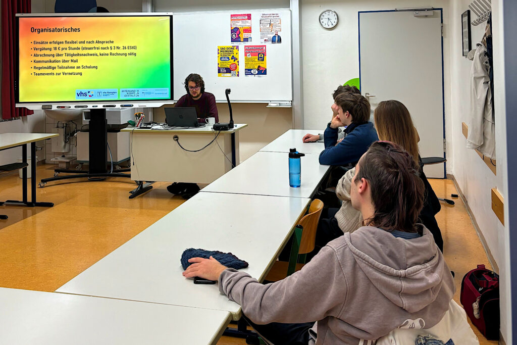 die Erste Teamer:innenschulung: Vorne an der Tafel sitzt Silvan Hecht die Koordinierungs- und Fachstelle und erklärt interessierten Zuhörern (rechts im Bild) Organisatorisches zum Teamer:innenpool