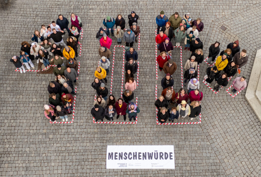 Drohnenbild von Oben. Es sind viele Menschen zu sehen die sich in der Form von "100 %" aufstellen.