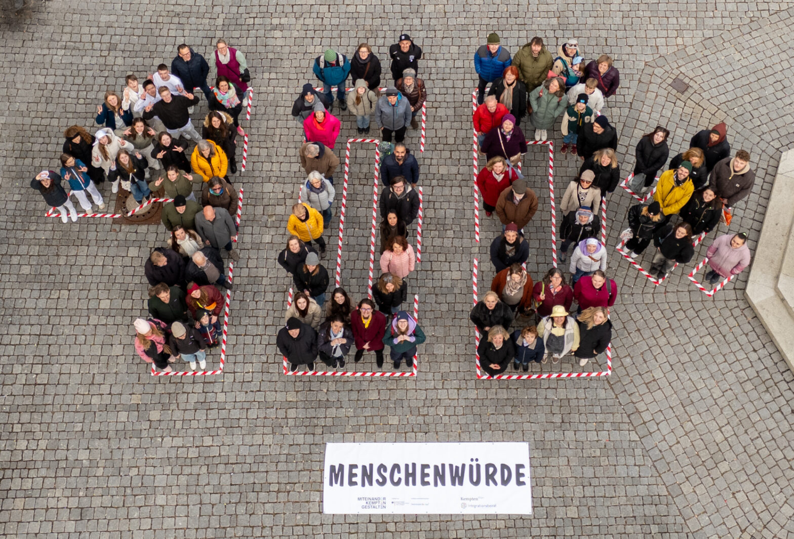 Drohnenbild von Oben. Es sind viele Menschen zu sehen die sich in der Form von "100 %" aufstellen.