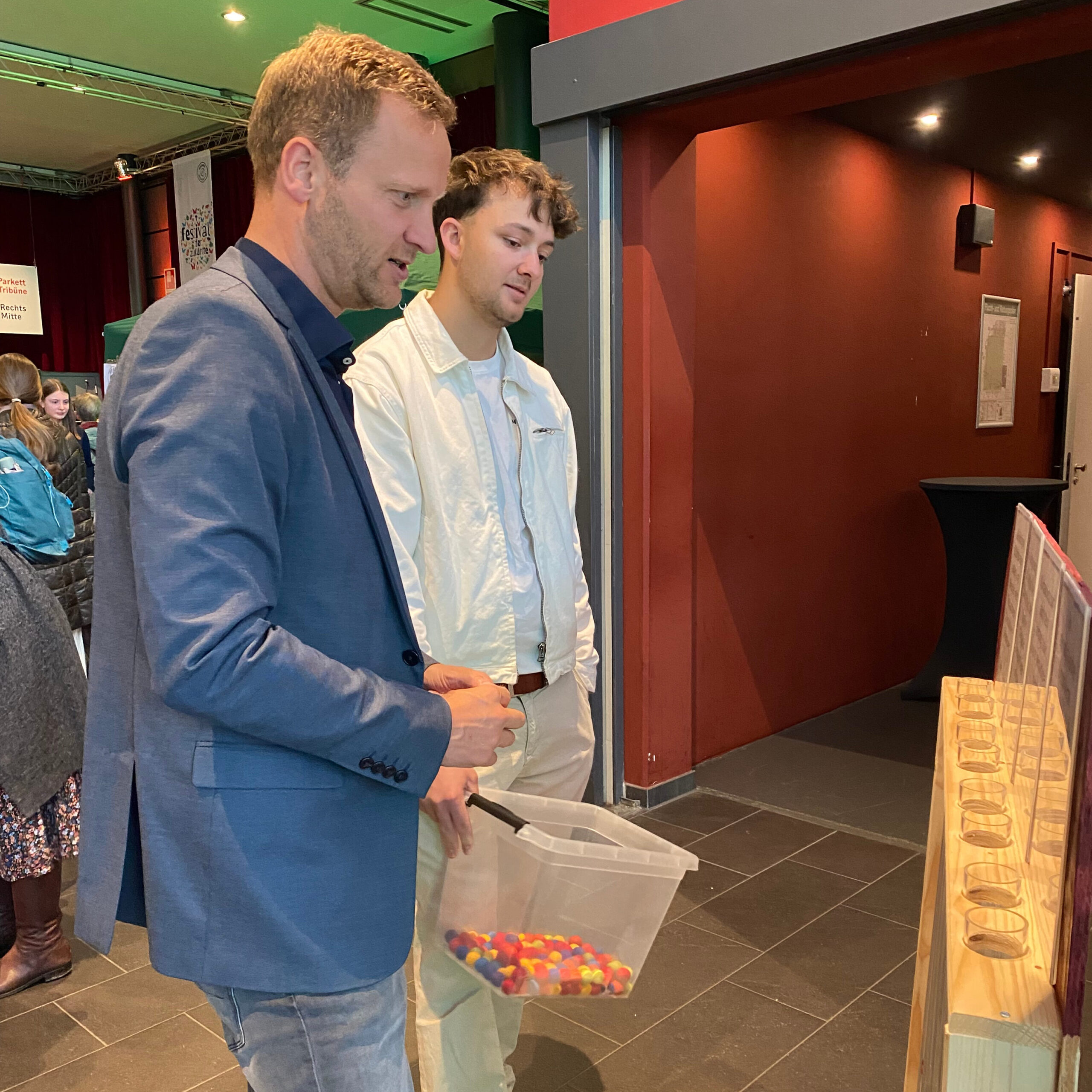 Oberbürgermeister Christian Schoch steht gemeinsam mit Demokratie-leben!-Teamer Nicolas Hefele vor der Abstimmungsstation beim Zukunftsfest. Schoch überlegt, wo er sein Bällchen hineinwerfen soll.