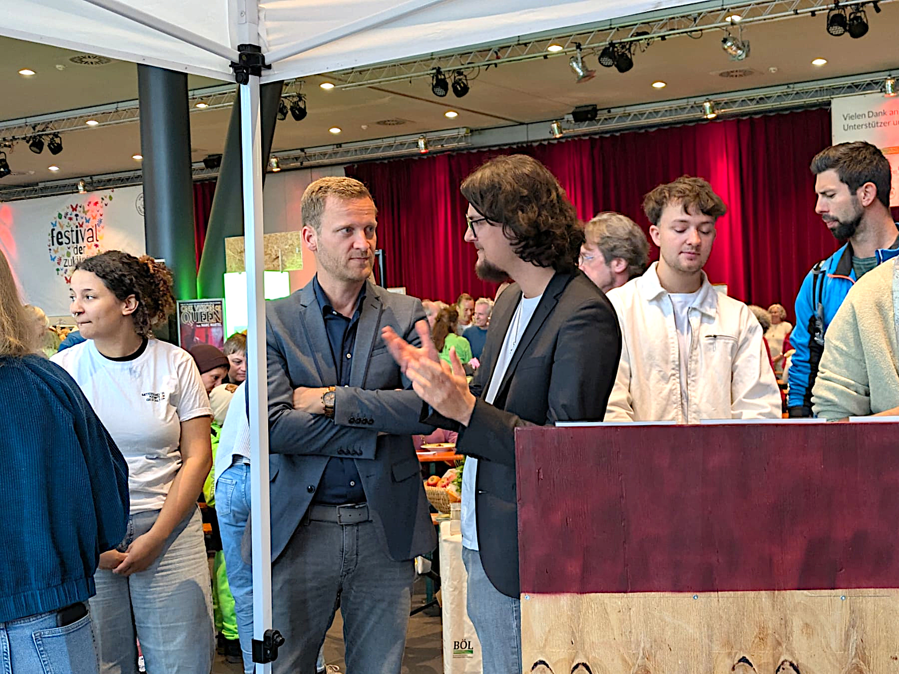Am Stand von „Demokratie leben!“ kommen Besucherinnen und Besucher beim Zukunftsfest miteinander ins Gespräch. Diverse Menschen stehen um unseren Stand